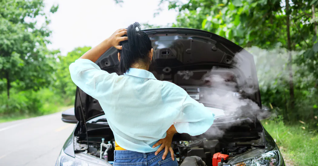 A woman looks into the steaming engine of her car