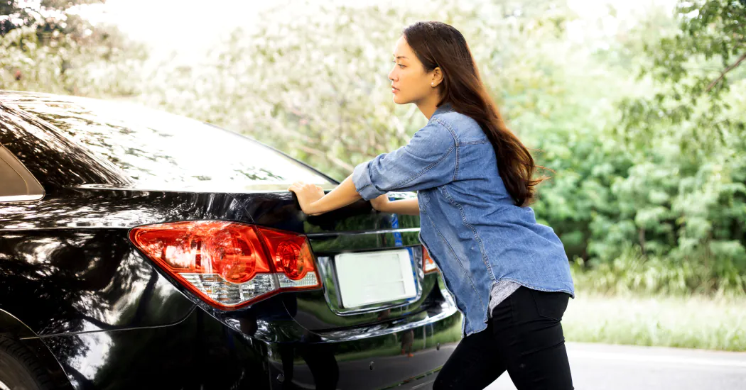 A woman pushes a car along the road