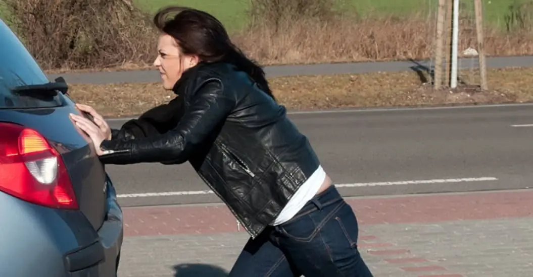 Woman struggling to push start her car on the road