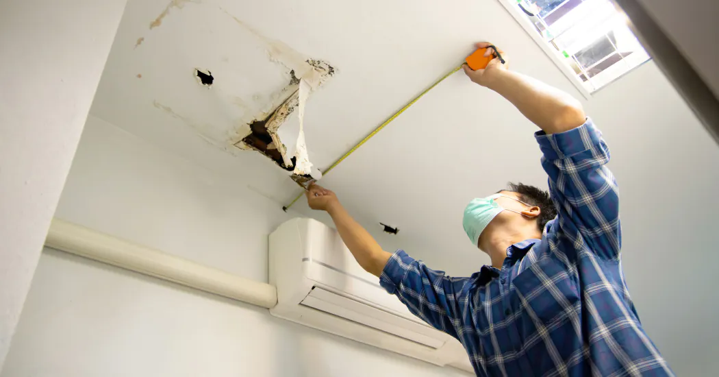 A man measures water damage to a ceiling