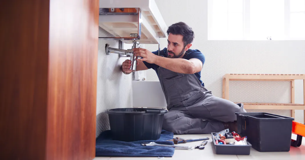 A plumber repairs a sink's pipes