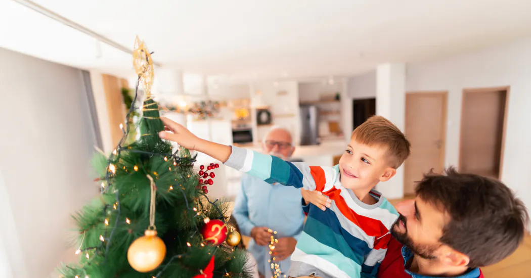 Dad lifts son to hang decorations on a Christmas tree
