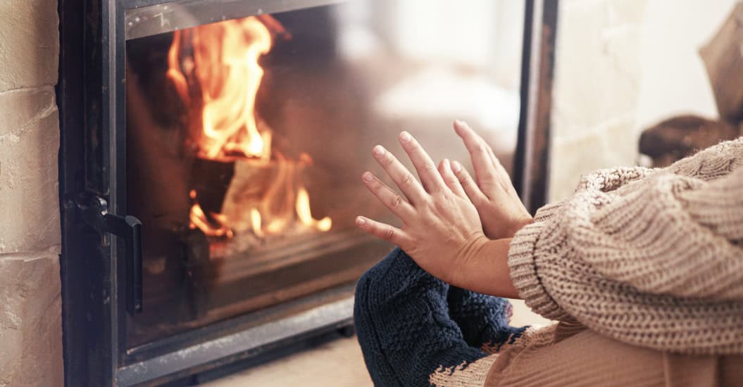 Woman warming up hands and feet next to fireplace