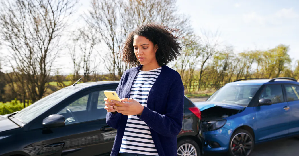 a concerned-looking woman checks her phone with a nose-to-tail car collision in the background