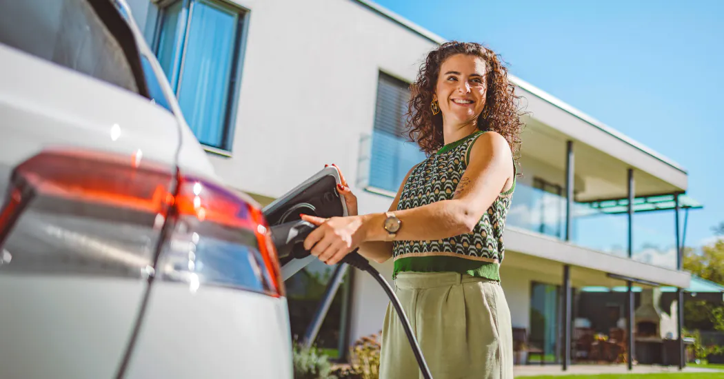 a smiling woman charges her EV at home