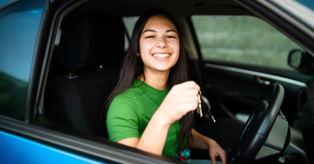 a young woman holding car keys smiles from the driver's seat